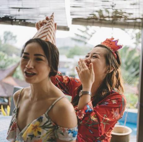 vaļsirdīgs brīdis, kurā aziātu ķīniešu sieviete palīdz māsai piesiet ballītes cepuri, gatavojoties dzimšanas dienas svinību pasākumam