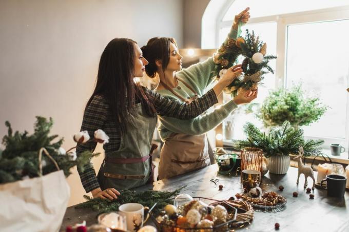 divas sievietes gatavo Ziemassvētku vainagu, izmantojot svaigus priežu zarus un svētku rotājumus